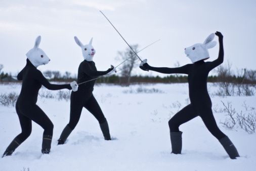 humans wearing rabbit masks while fencing