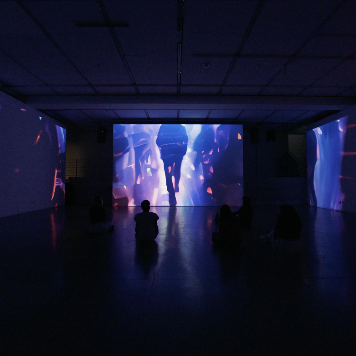 AI visuals projected on three walls with people sitting on the floor